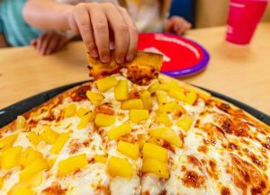 kid's hand picking up slice of pineapple pizza