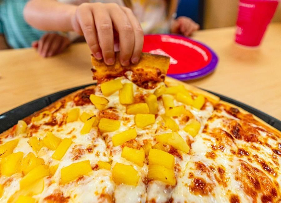 kid's hand picking up slice of pineapple pizza